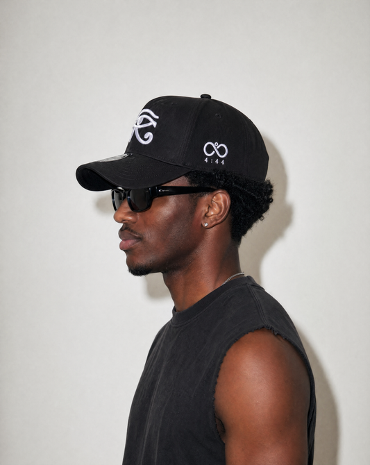 Man wearing a black cap with white logo and sunglasses on a plain background