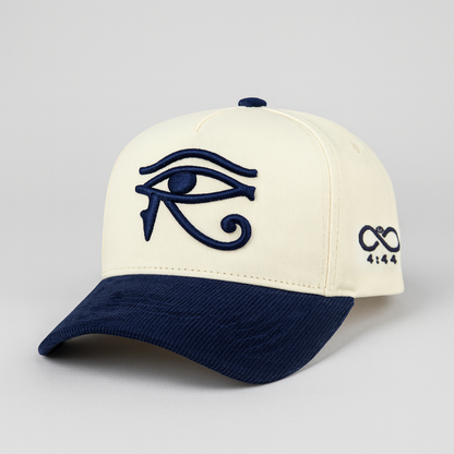 Cream-colored cap with navy blue eye of horus design and symbol on a light gray background