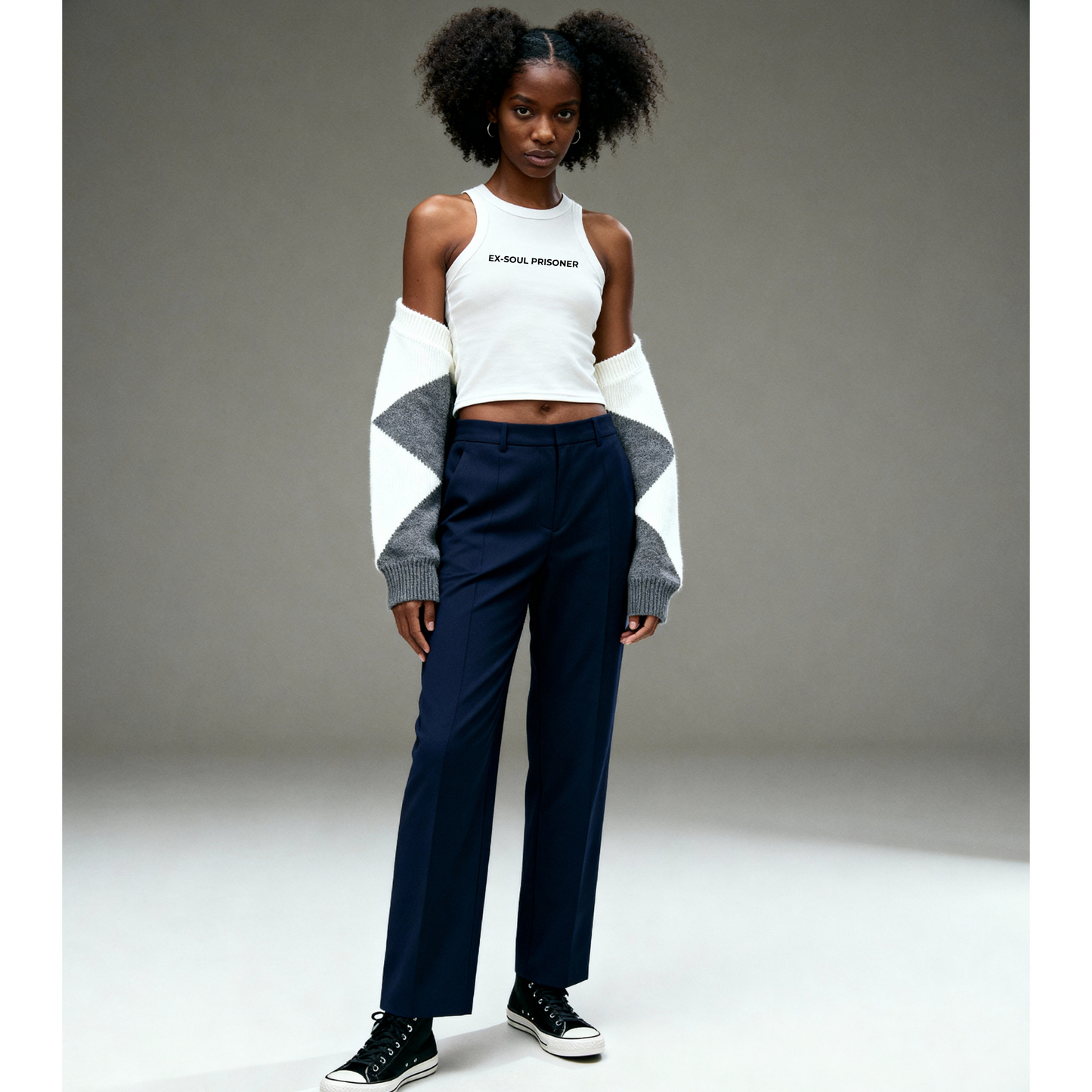 Person wearing a white crop top and navy pants with a gray sweater on a plain background