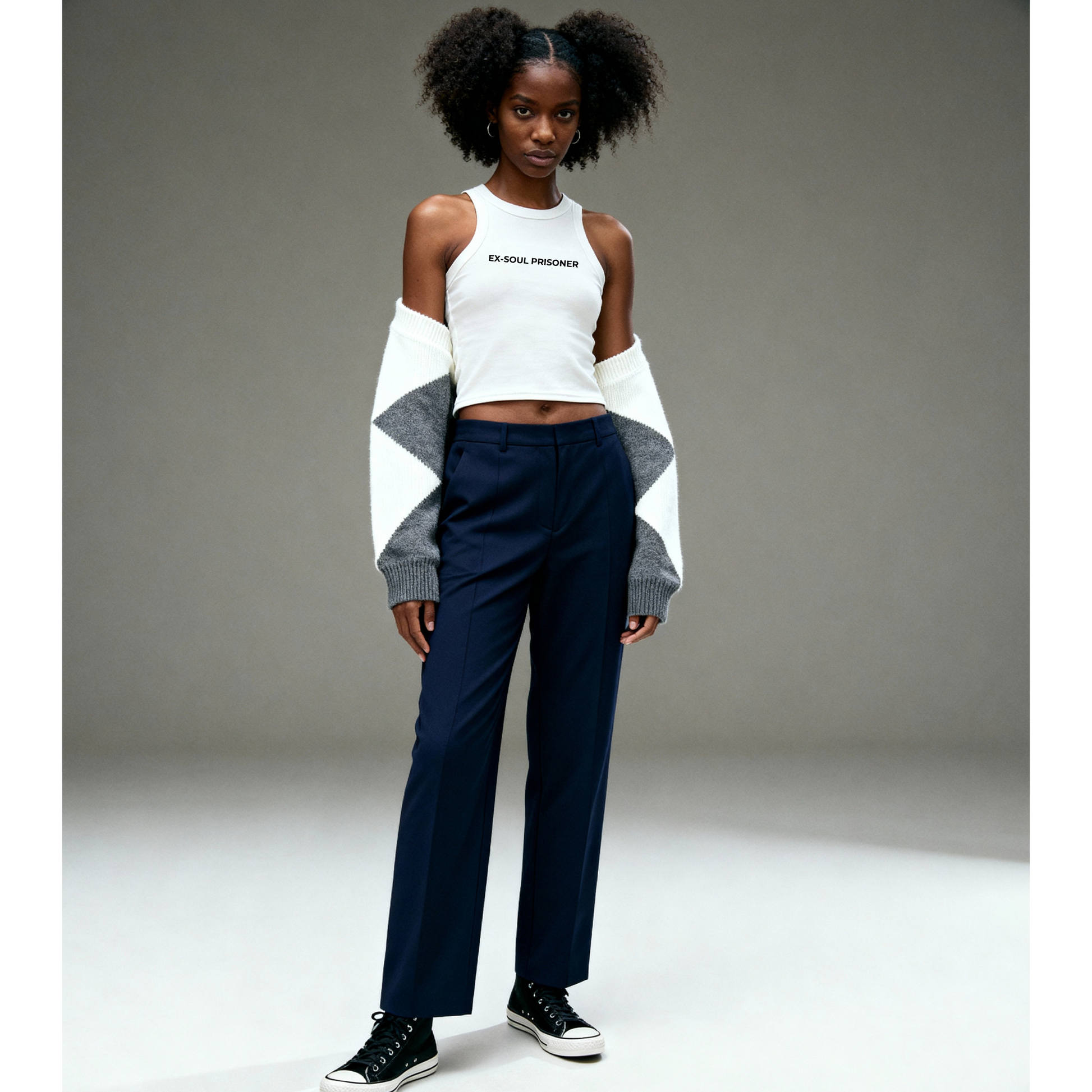 Person wearing a white crop top and navy pants with a gray sweater on a plain background