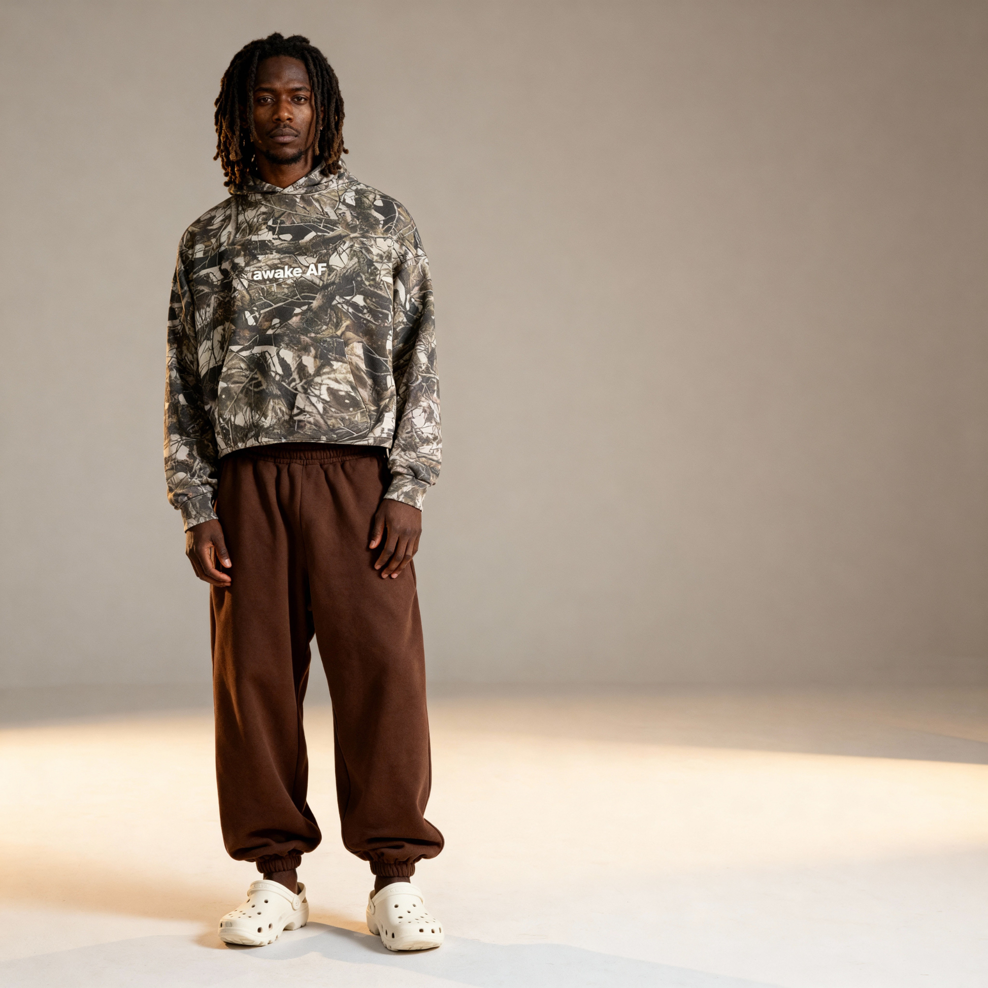 Person wearing a camouflage hoodie and brown pants on a neutral background