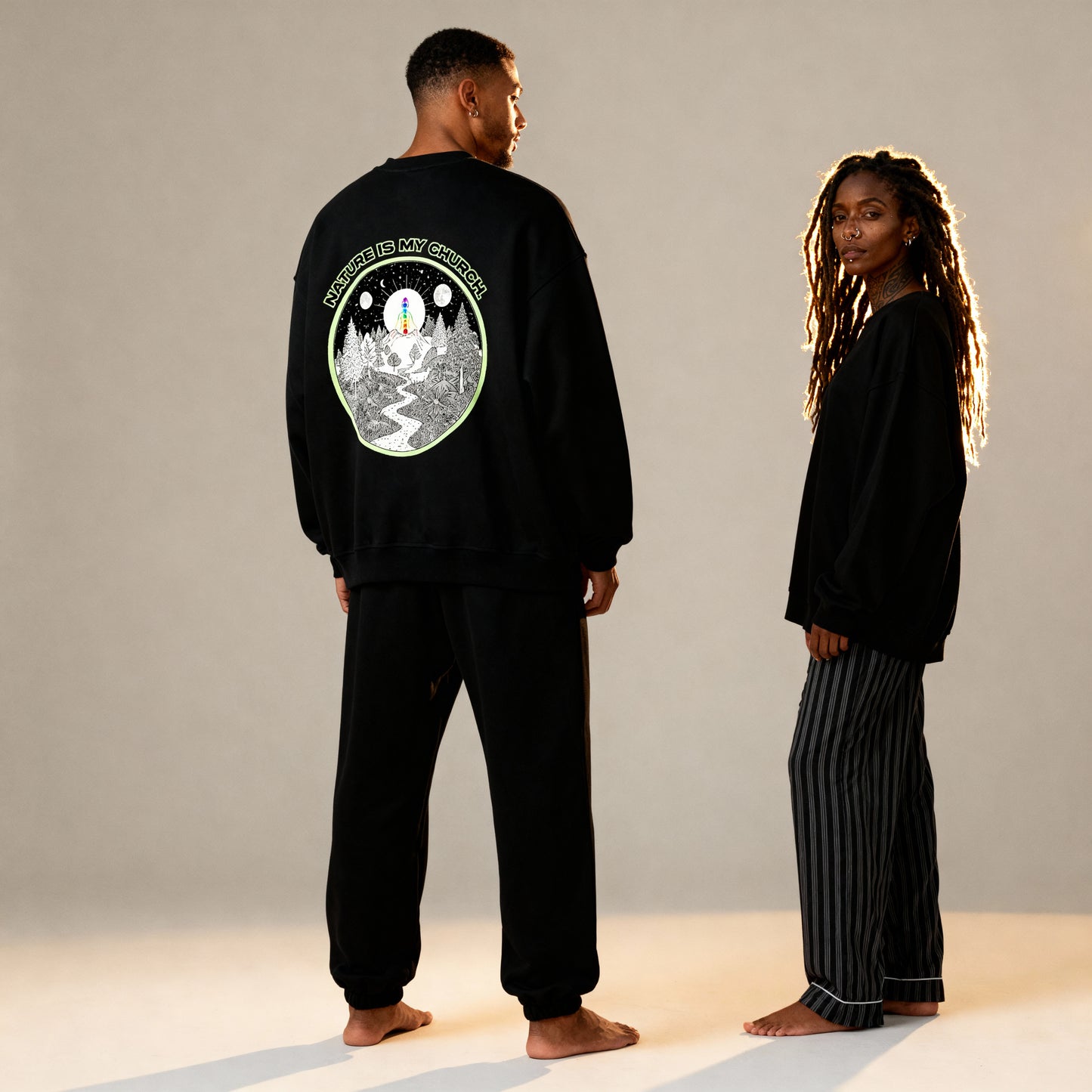 Two people wearing black outfits with a design on the back, standing against a neutral background.