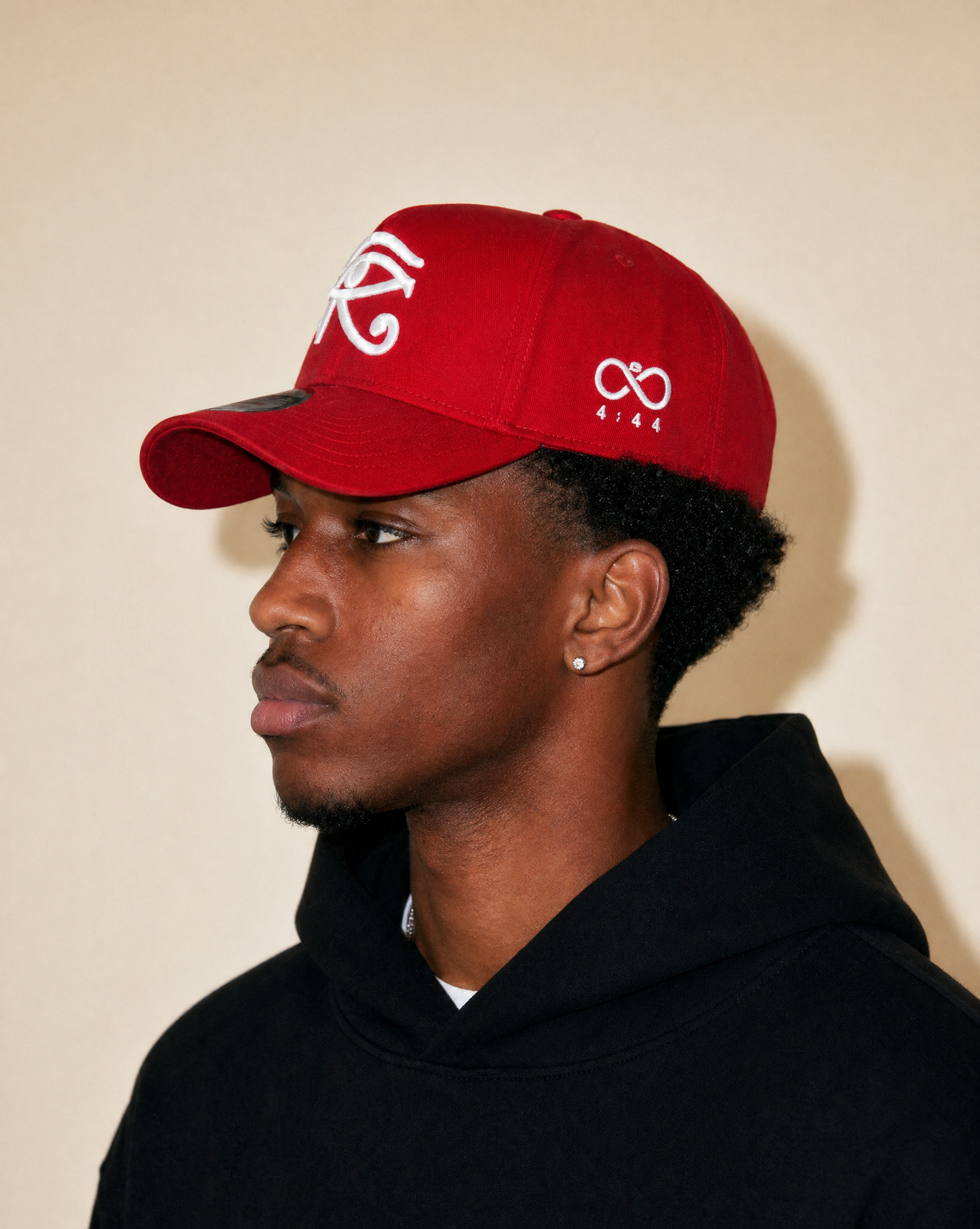 Person wearing a red cap with white logo against a beige background