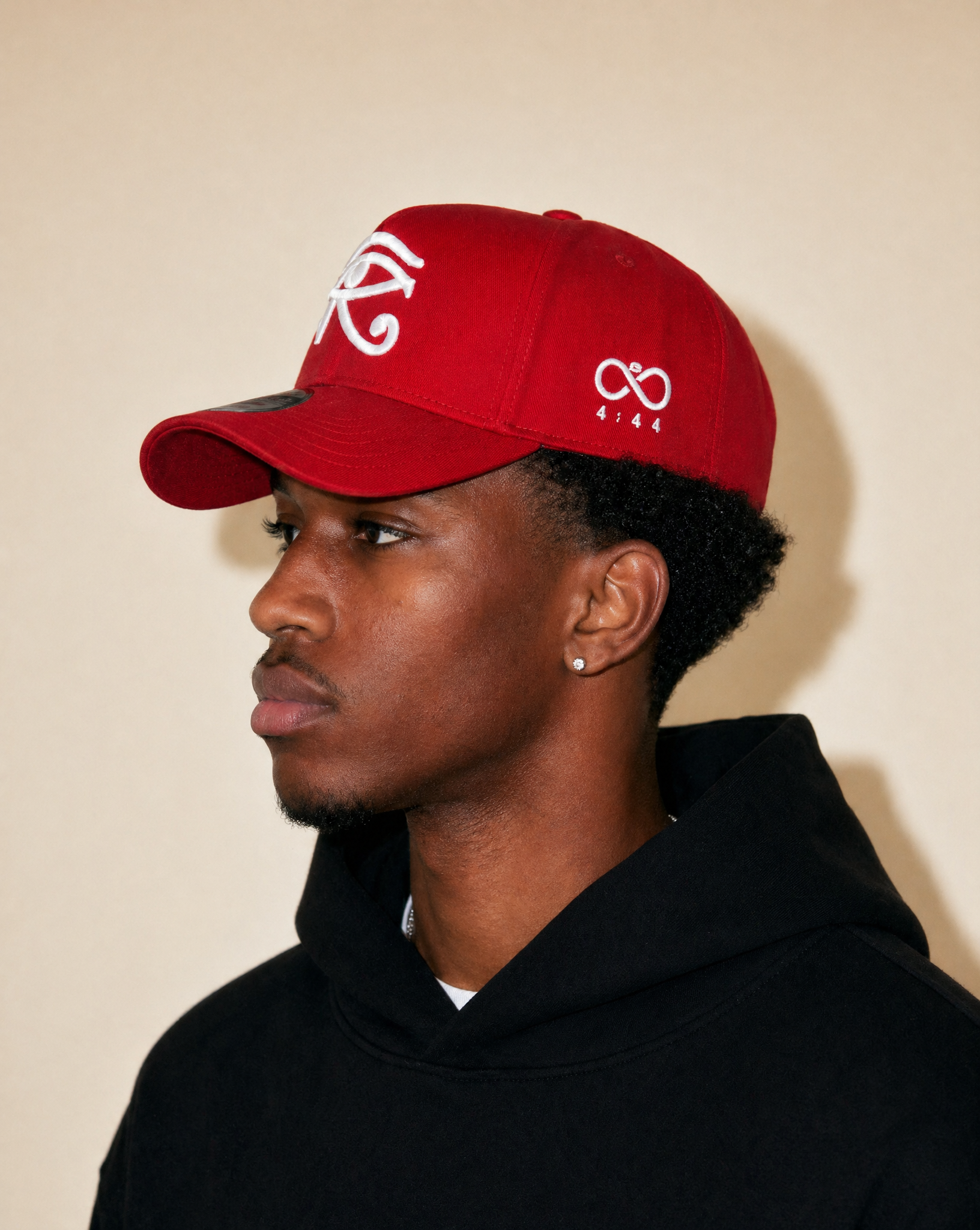 Person wearing a red cap with white logo against a beige background