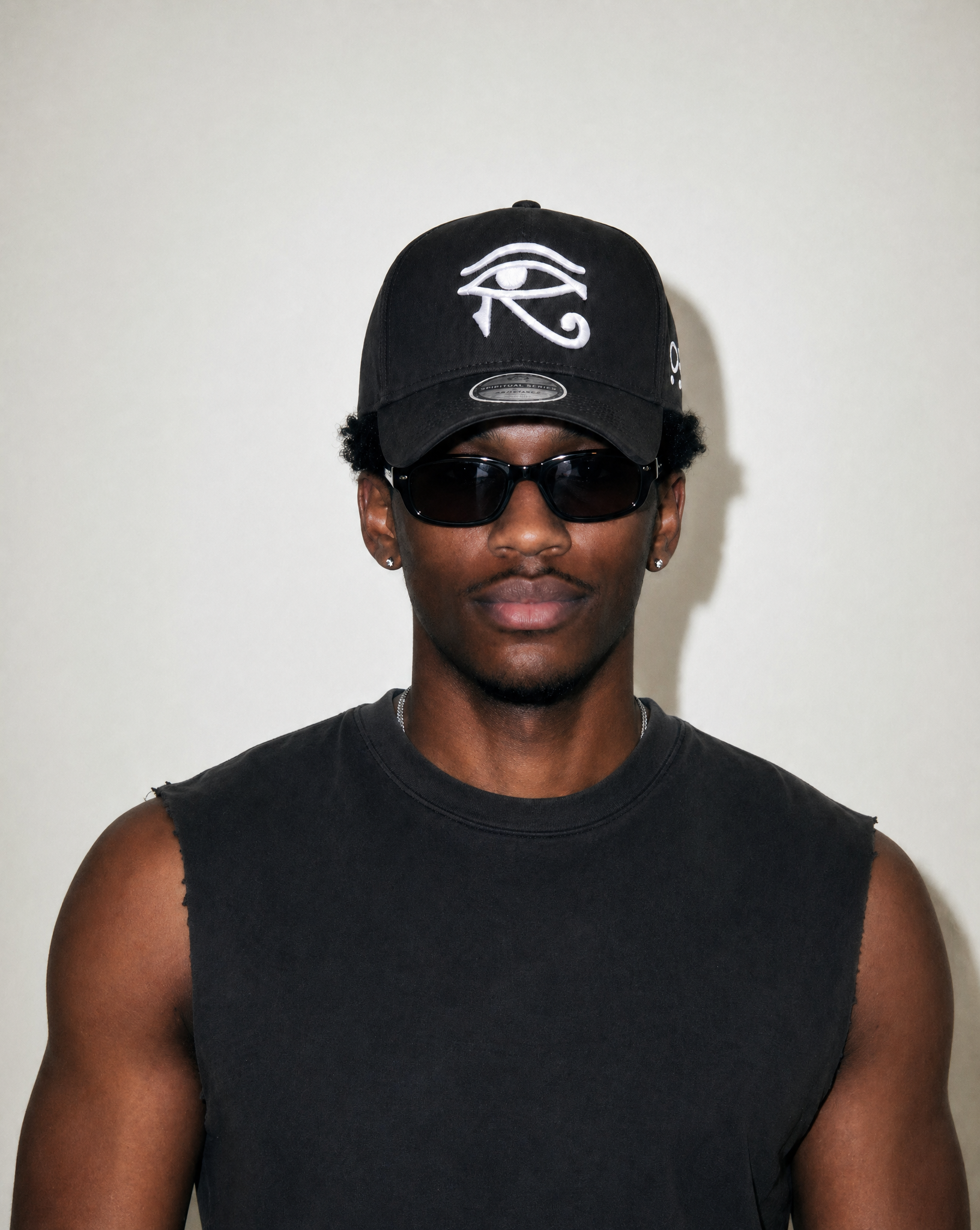 Person wearing a black cap with a white symbol and sunglasses against a plain background