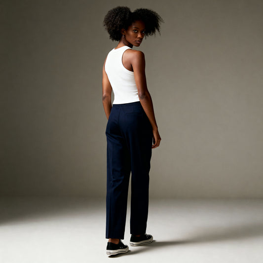 Woman wearing a white tank top and navy pants against a neutral background