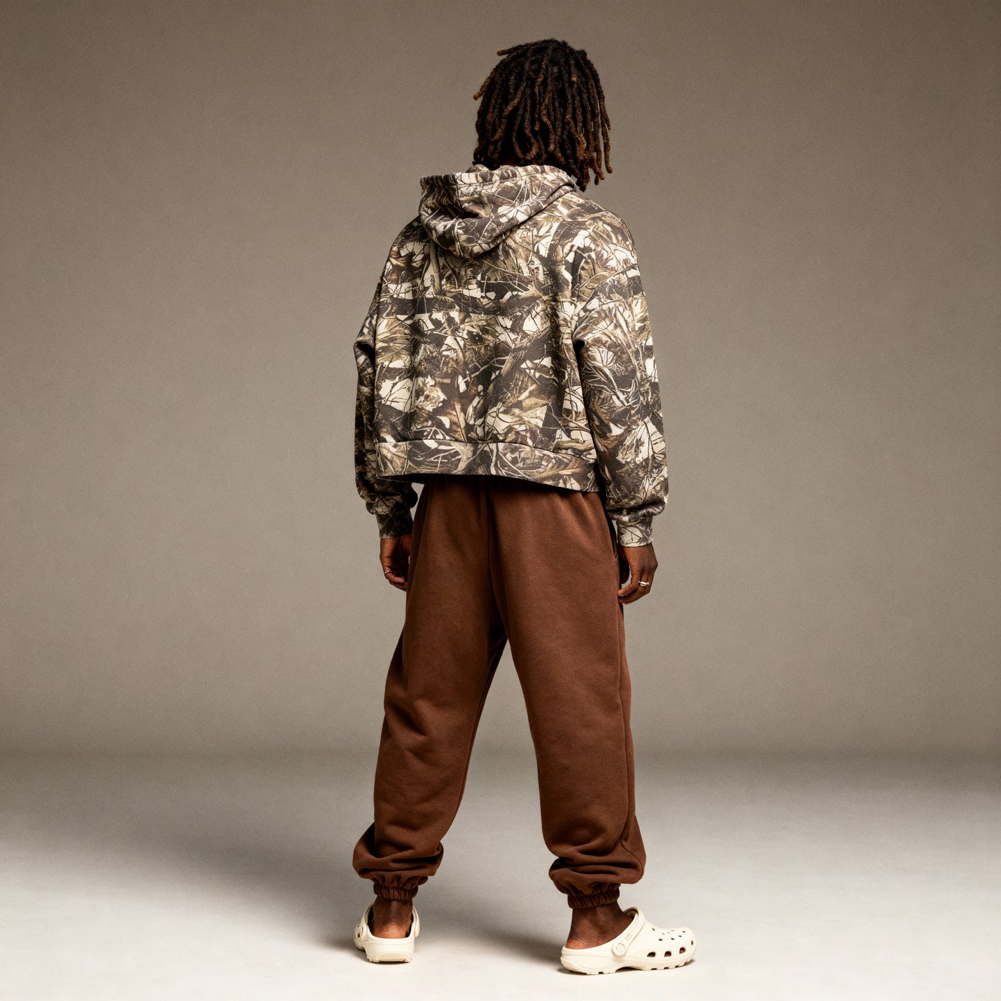 Person wearing a camouflage jacket and brown pants against a plain background