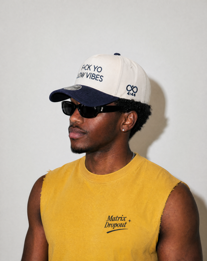 Man wearing a white and navy cap with text, sunglasses, and a yellow sleeveless shirt with text.