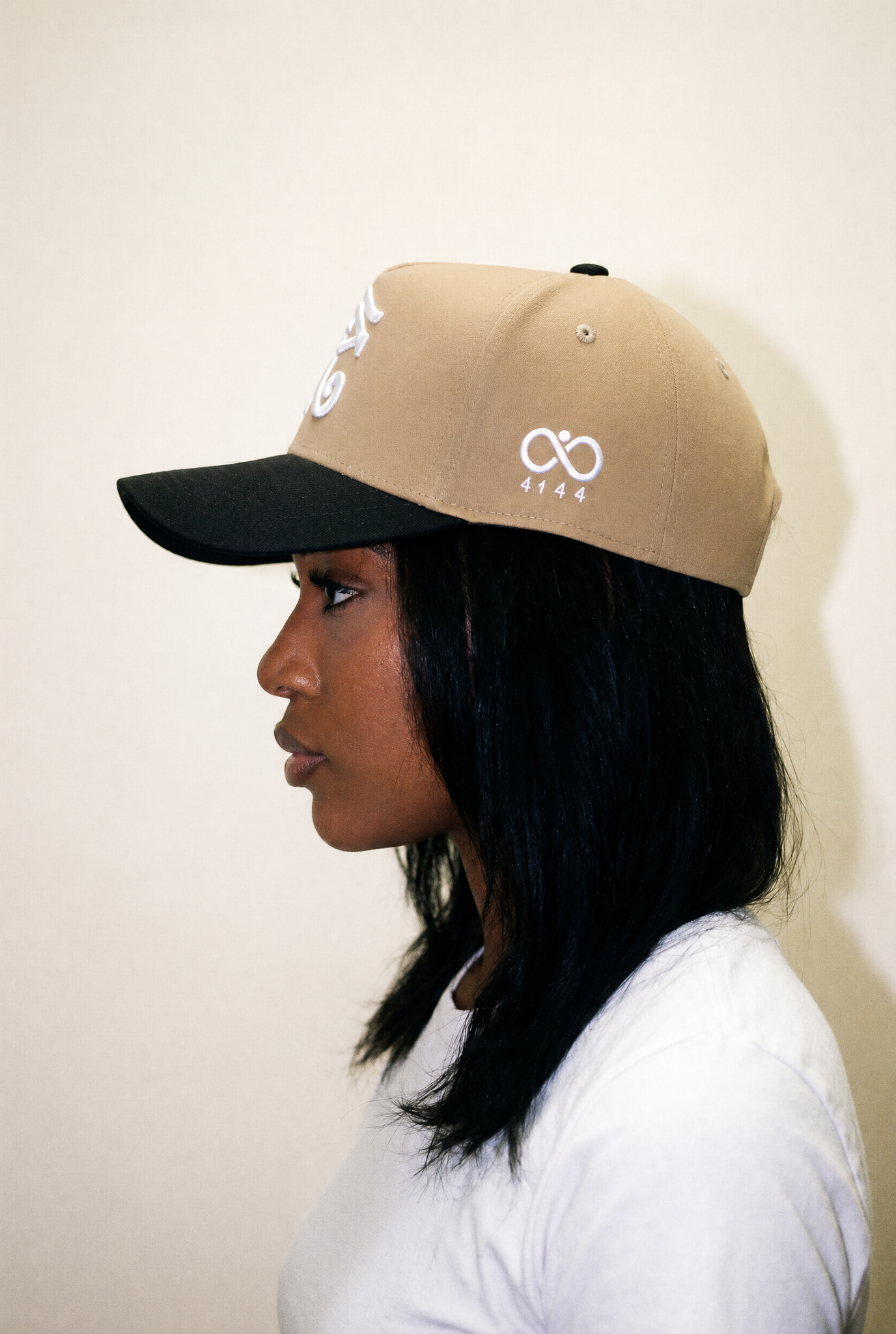 woman wearing a beige and black cap with a logo on a plain background